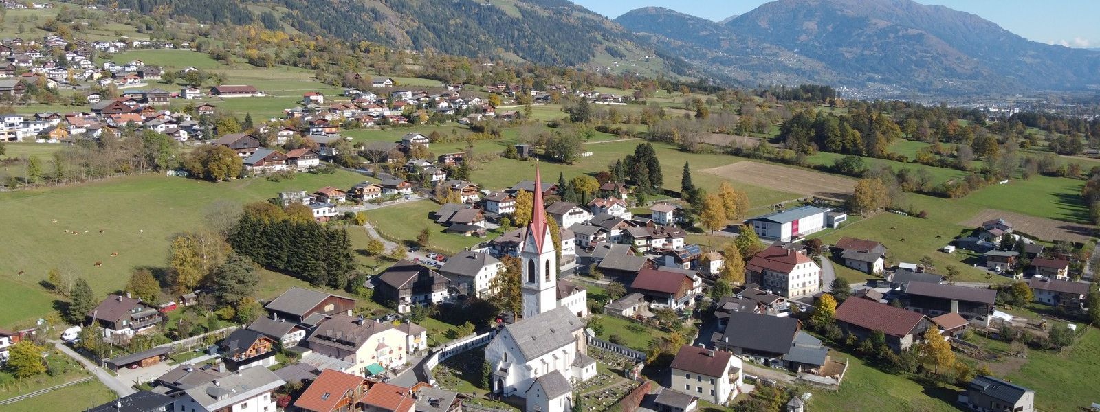 Luftaufnahme im Herbert der Gemeinde Oberlienz mit der Kirche im Zentrum.