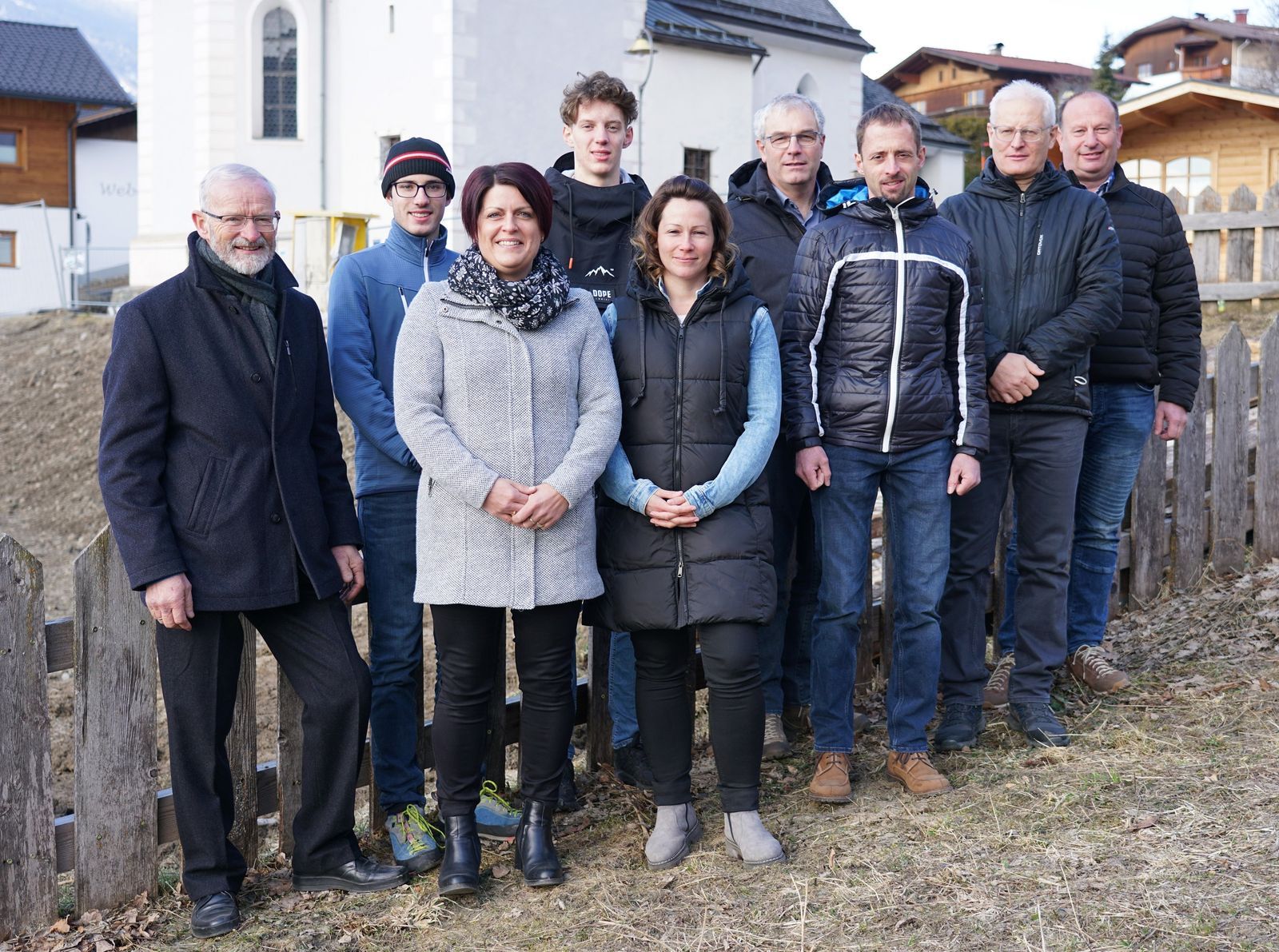 9 Personen, darunter 2 Frauen, stehen in 2 Reihen vor der Kirche