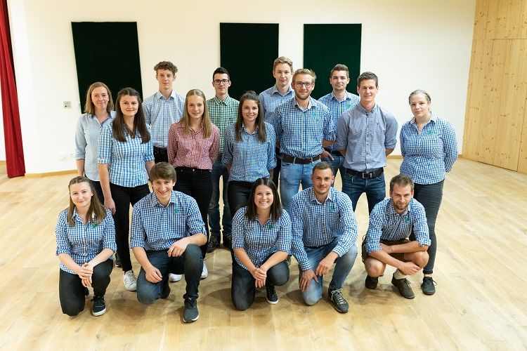 16 Jugendliche in einem Saal. 5 hocken, der Rest steht in 2 Reihen dahinter