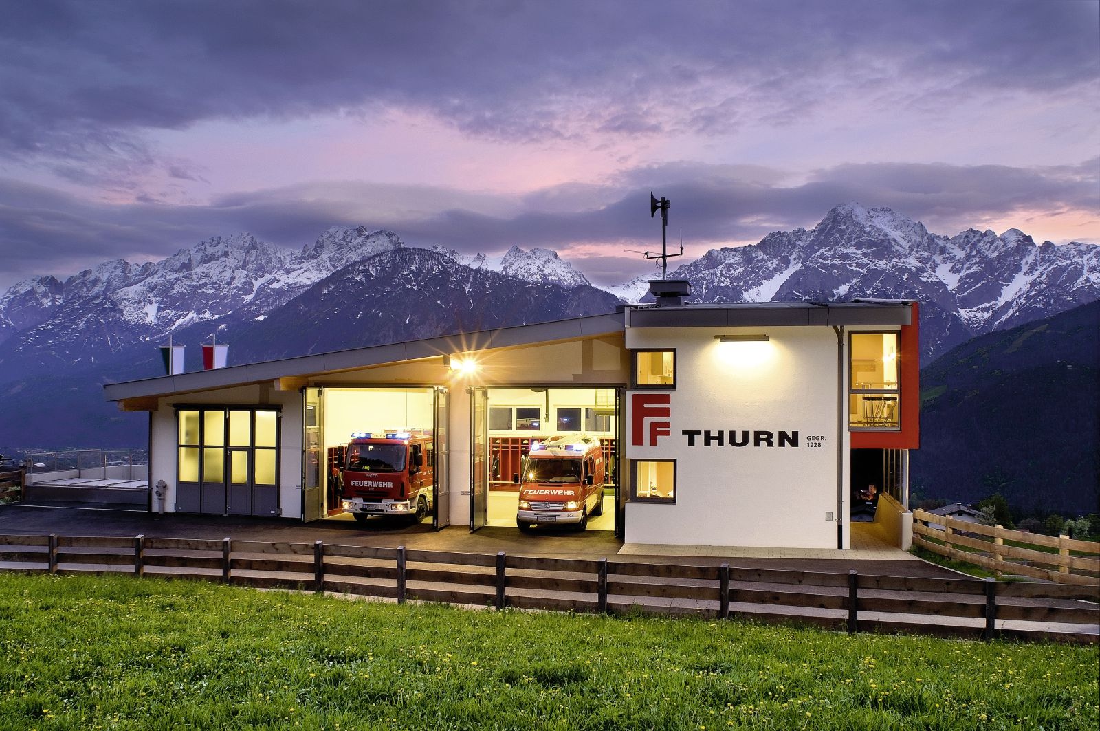 Feuerwehrgebäude mit 2 Feuerwehrautos die in der Garage stehen.