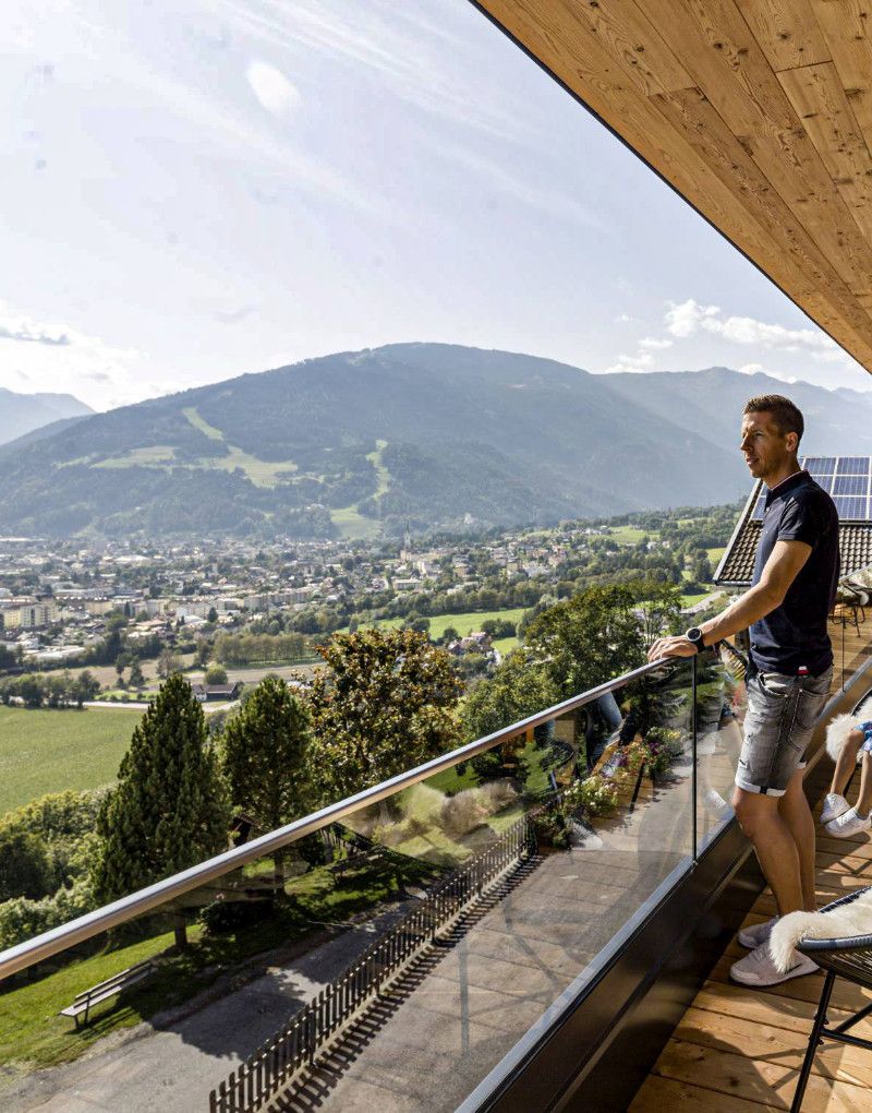 Ein Mann steht im Sommer am Balkon seiner Unterkunft und schaut in die schöne Landschaft 