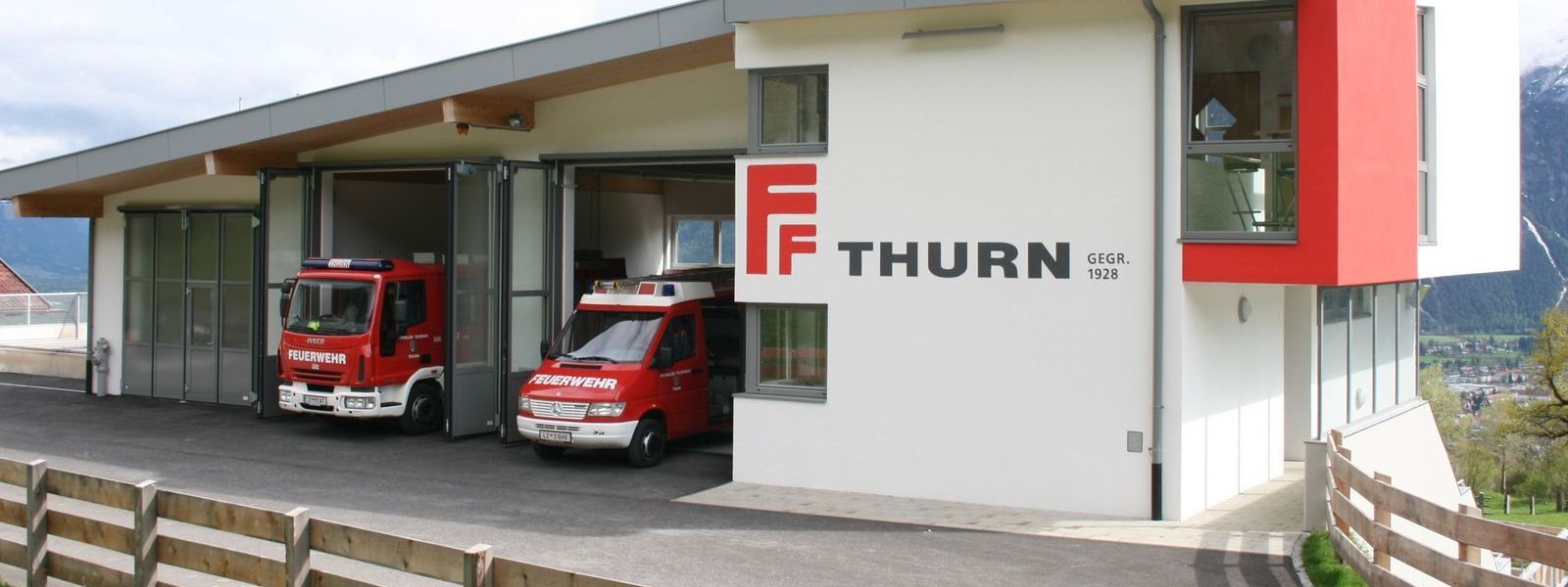 Feuerwehrgebäude mit 2 Feuerwehrautos die in der Garage stehen.