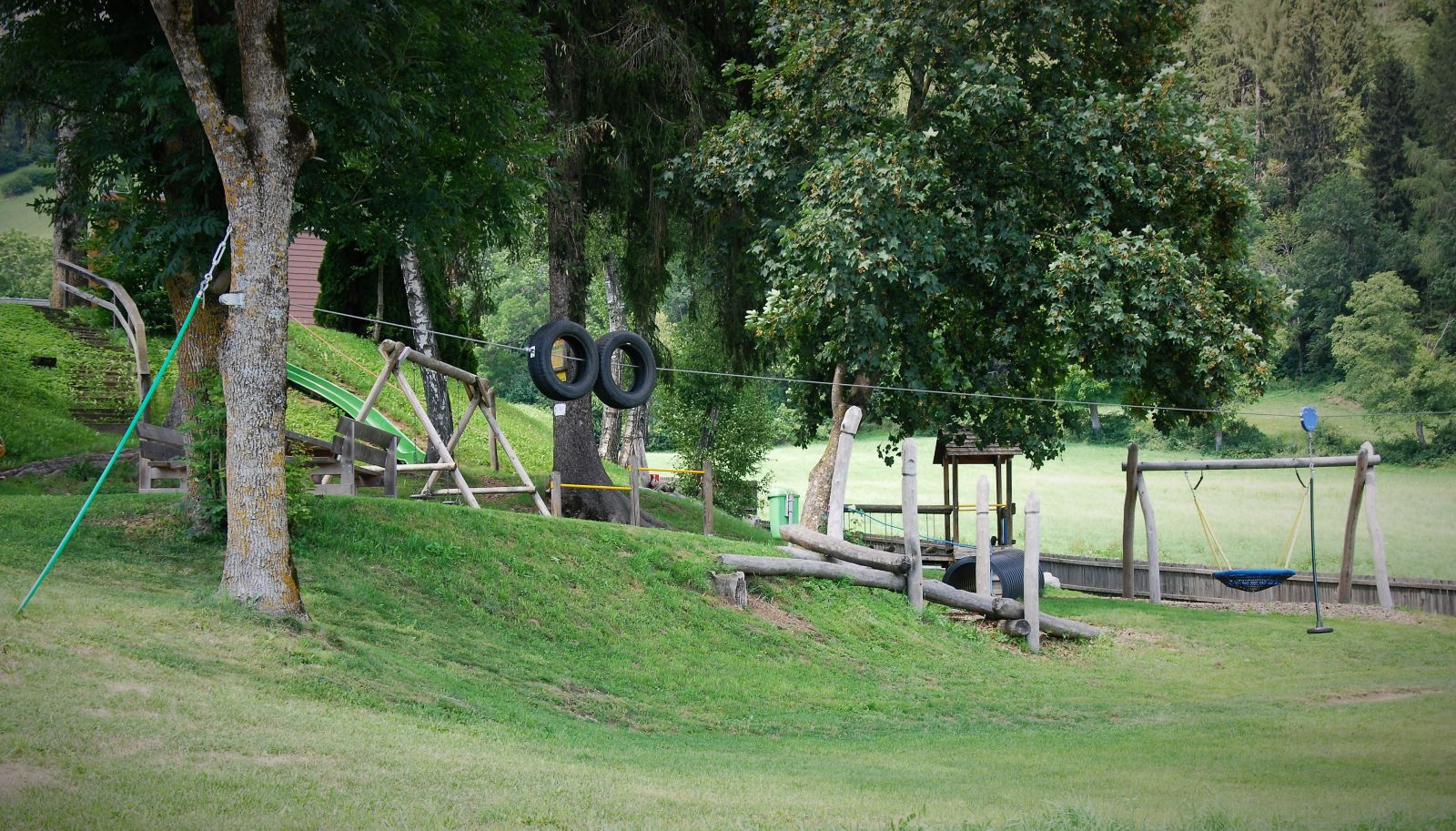 Ein Spielplatz mit verschiedenen Geräten aus Holz, ein Holztisch mit 2 Holzbänken