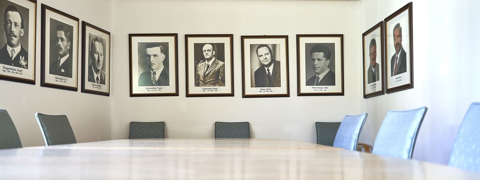 Sitzungszimmer. Großer Tisch mit Stühlen und Portraits der bisherigen Bürgermeister an der Wand